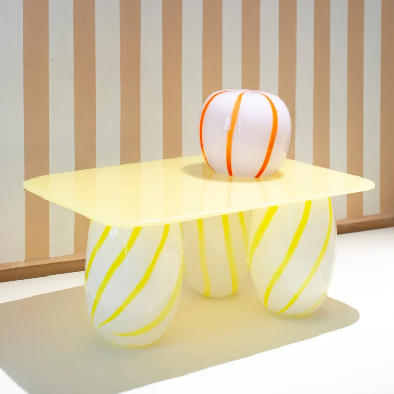 Yellow Candy Sofa Table by Studio Berg in front of a striped wall, a round striped orange and white glass vase on top