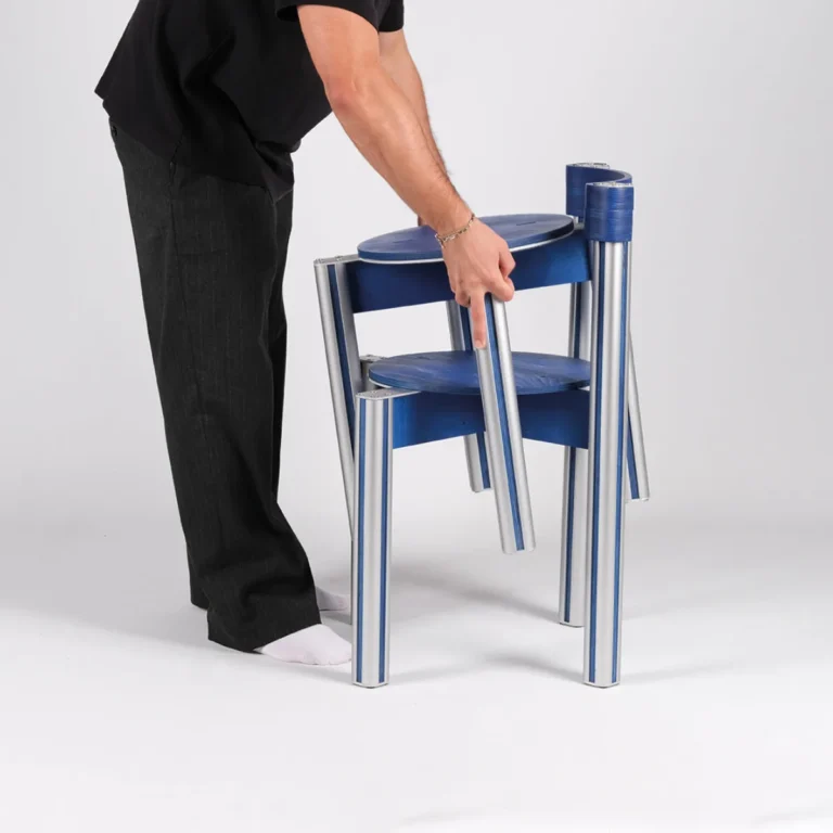 Sigma Chair by 301 Design Studio, a person in black lifting a blue chair stacked on another, aluminum legs showing