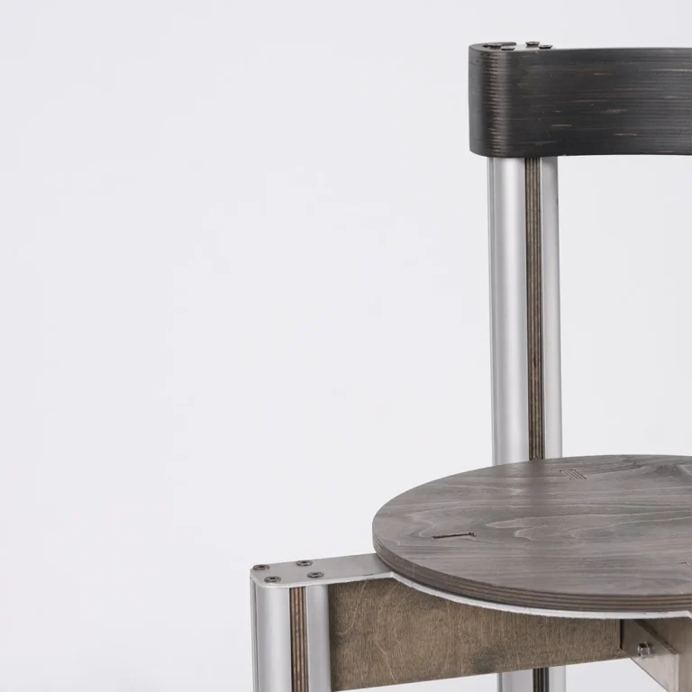 Close-up of the Sigma Chair's grey birch seat, dark backrest and screwed aluminum leg joint, by 301 Design Studio