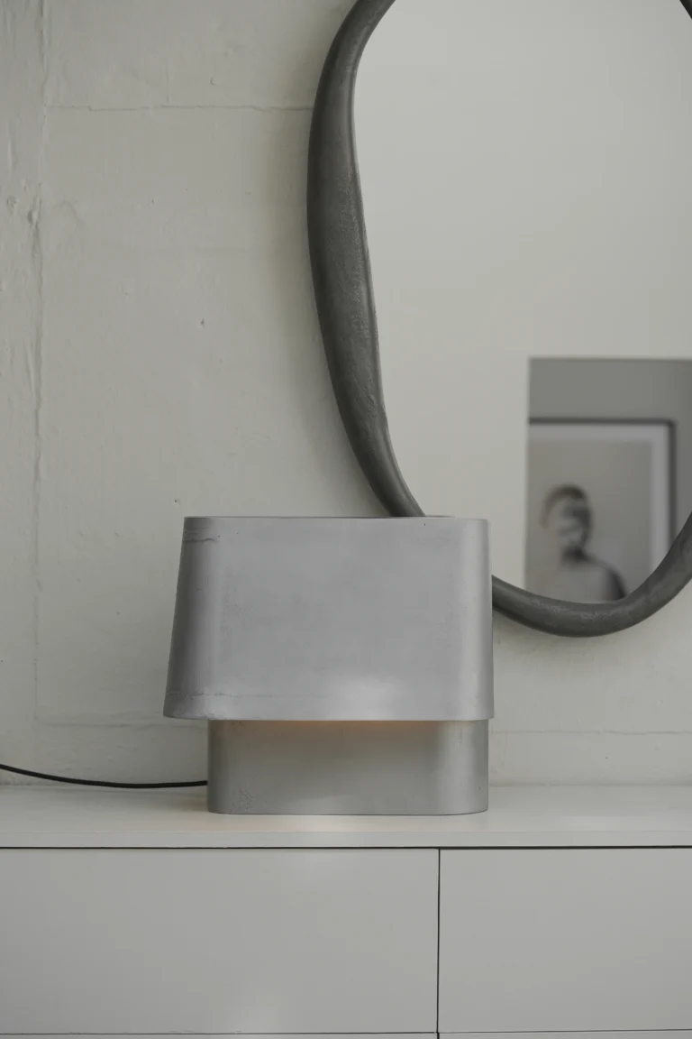 Mirror Perfumer by Vogel Studio above a white sideboard, behind a lit metal table lamp with a black cord