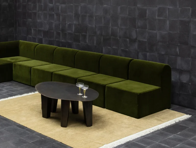 Paris Coffee Table by Vogel Studio in a lounge, on a cream rug in front of a green velvet modular sofa, two coupe glasses on top