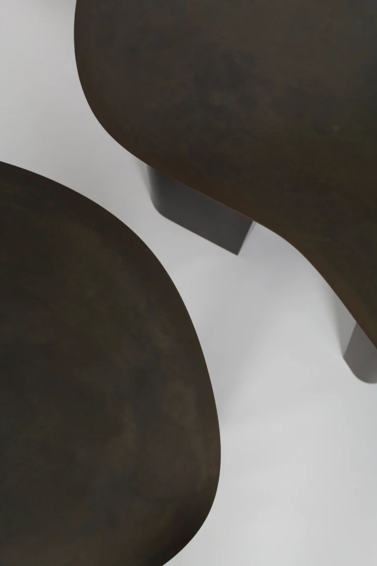 Close-up of the Paris Coffee Table's blackened steel tops, two curved edges showing the mottled patina against a pale background