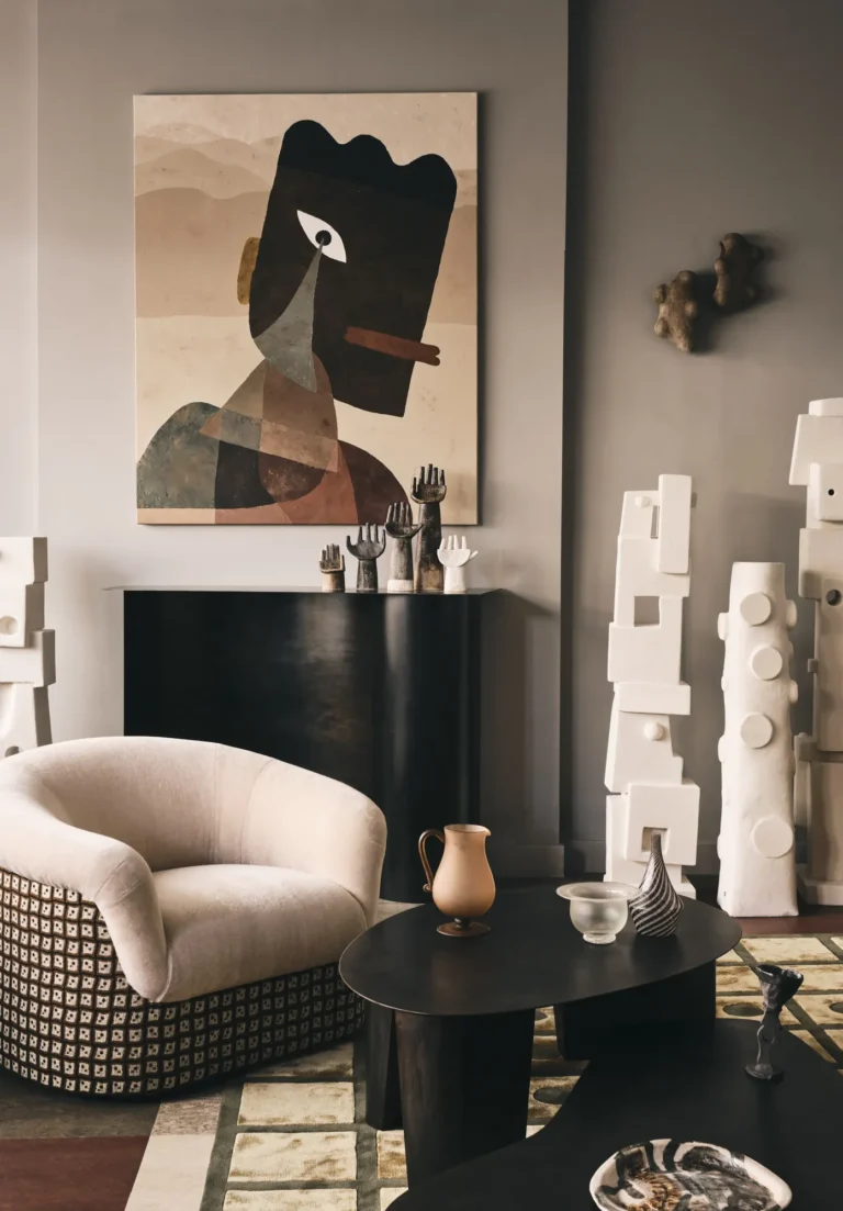 Paris Coffee Table by Vogel Studio in a living room, beside a cream armchair, white sculptures and a large painting