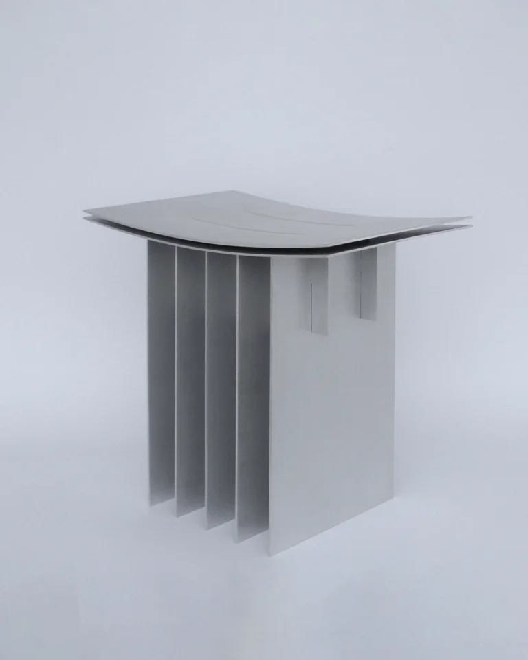 Brush Stool by SESTRA, aluminum stool with a curved double seat on parallel vertical fins, on a plain background
