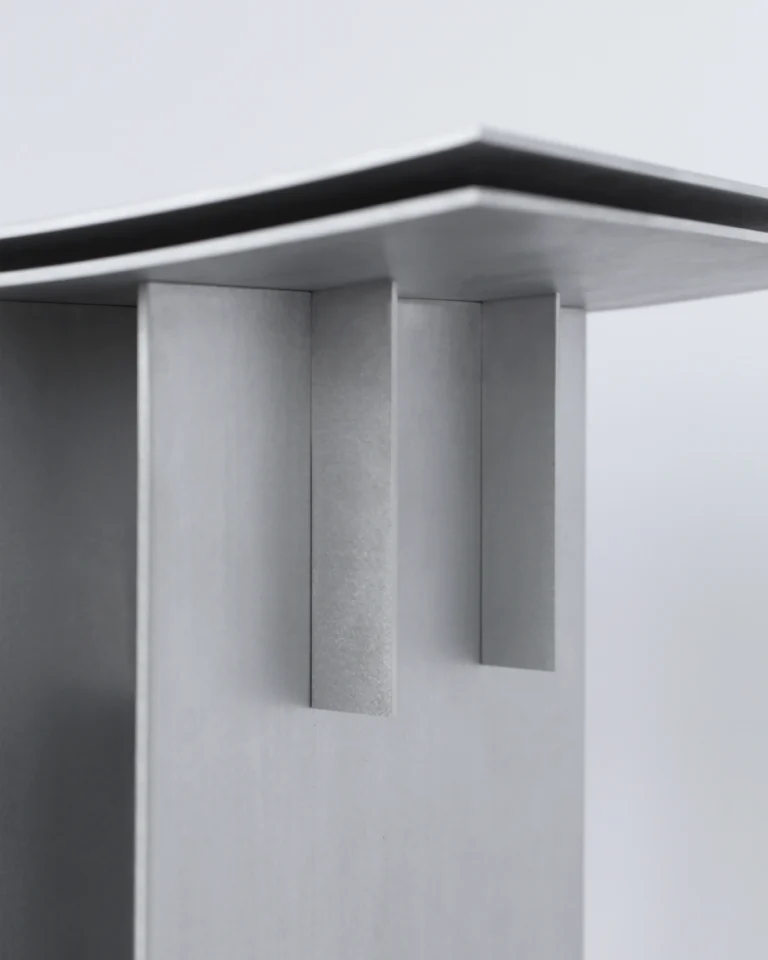 Close-up of the Brush Stool's two vertical tabs joining the brushed aluminum fin to the layered curved seat