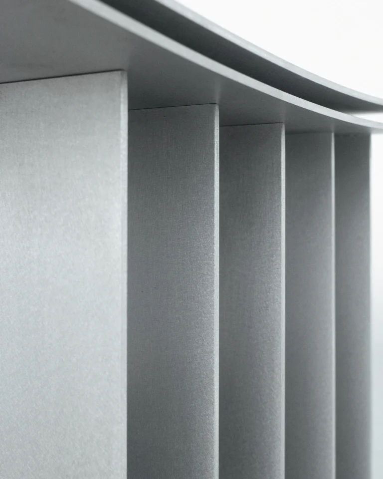 Close-up of the Brush Stool's grainy matte aluminum fins stepping beneath the curved seat