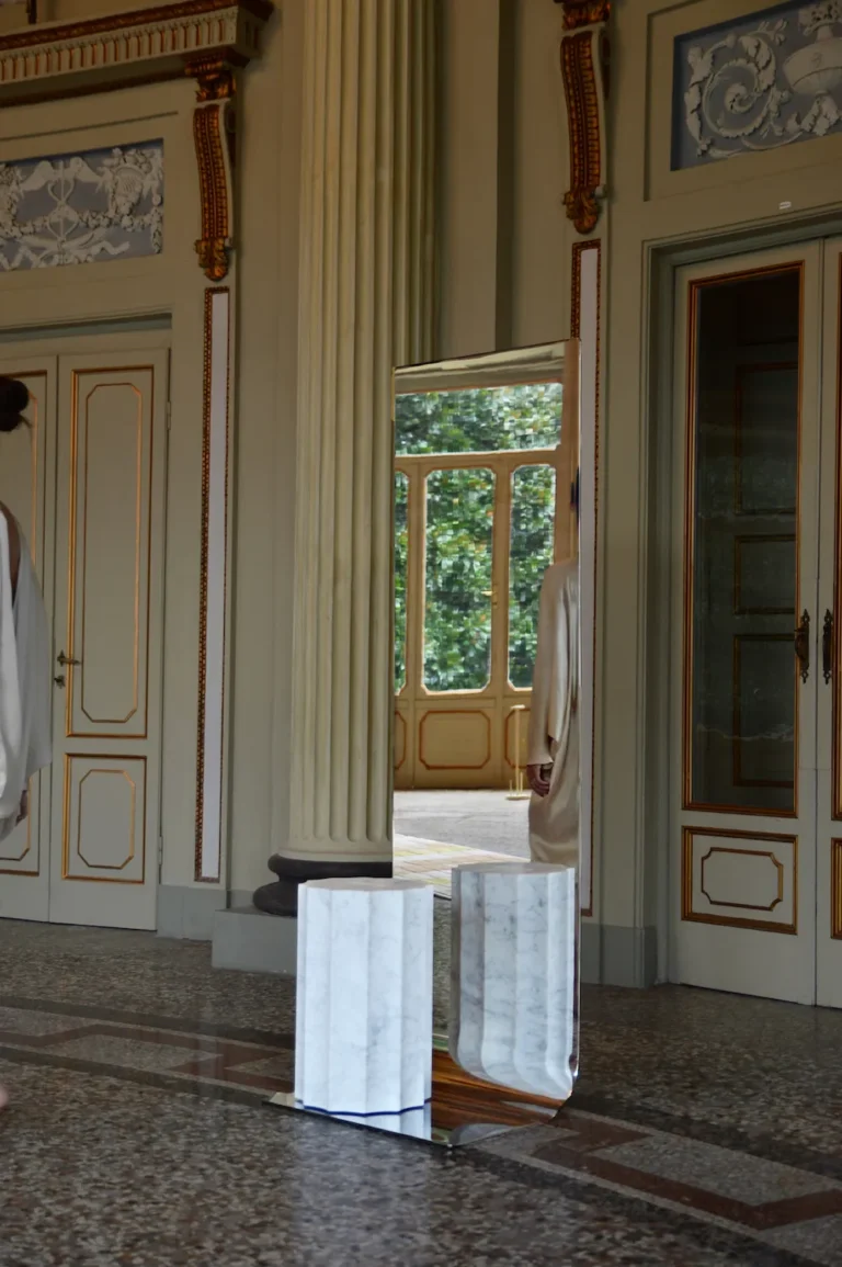 Meditations - Full-Length Mirror by STUDIO VON SCHOENEBECK in a columned period hall, reflecting a doorway and garden