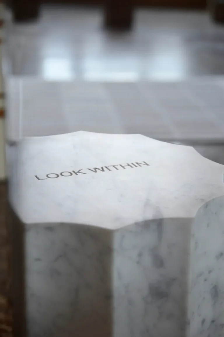 Close-up of the Meditations mirror's fluted marble top with the words LOOK WITHIN engraved, against a soft blurred background