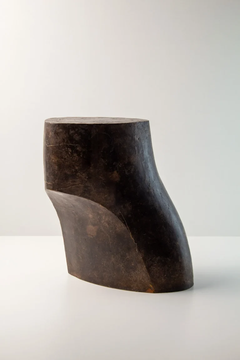 Palm Table I by Vogel Studio, dark raw finish bronze side table with a curved, leaning form, on a plain pale background