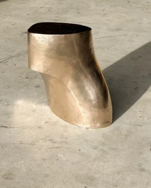 Palm Table I by Vogel Studio, polished bronze side table with a curved, leaning form, on a concrete floor