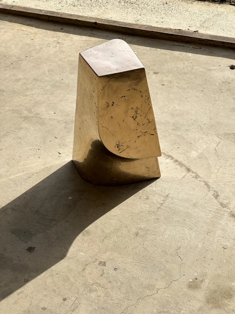 Palm Table Il by Vogel Studio seen from the side, the curved cut-away between the upper block and base in raking sunlight