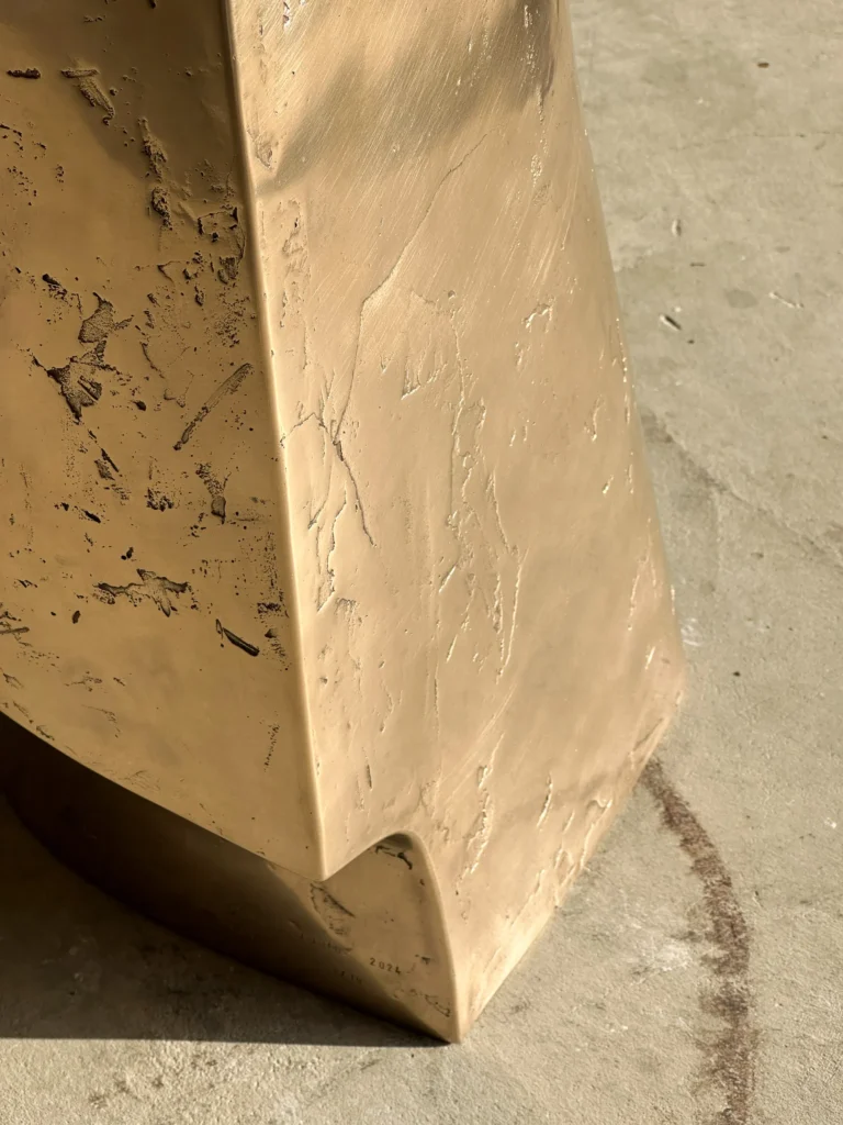 Close-up of the Palm Table Il's base, with its textured cast bronze surface, sharp edge and curved notch at the foot