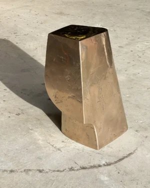 Palm Table Il by Vogel Studio, polished bronze side table with a tapered body and cut-away base, on a concrete floor