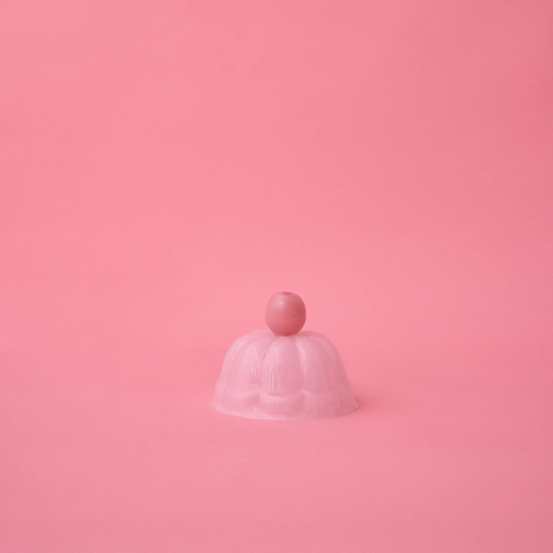 JELLO S hand-blown glass cloche in rose milk, shaped like a fluted jelly mold with a round knob, on a pink background, by STUDIO BERG